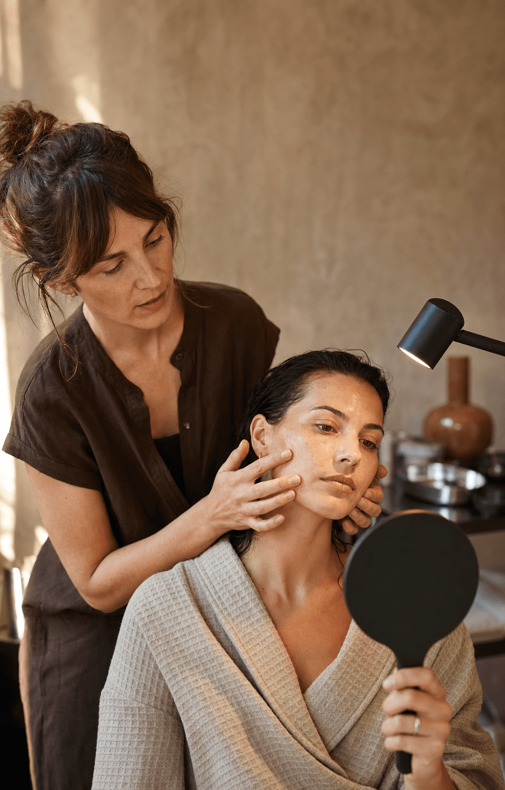 A skincare practitioner helping a client examine her skin